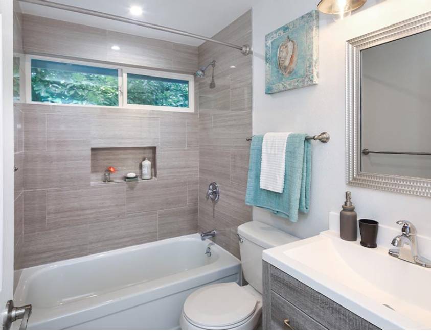 Modern bathroom with beige tiles, bathtub, and window with greenery view Modern bathroom with beige tiles, bathtub, and window with greenery view