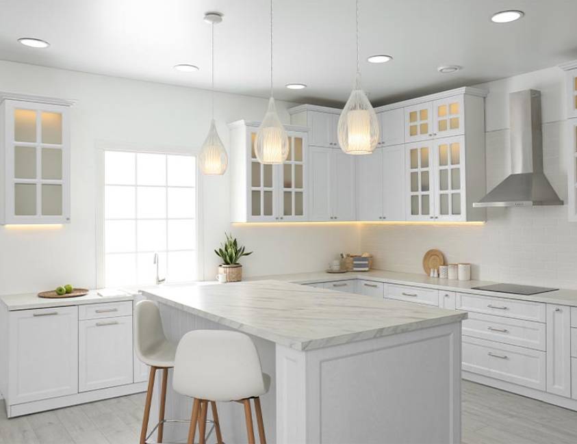 Modern kitchen interior with white cabinetry, marble countertops, and pendant lights Modern kitchen interior with white cabinetry, marble countertops, and pendant lights